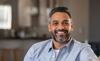 Man sitting on couch and smiling with dentures in Worcester