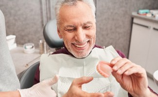 Man smiling while holding a mold of dentures