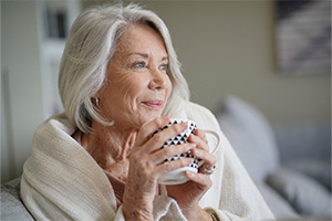 Senior woman sitting at home under a blanket and holding a coffee mug