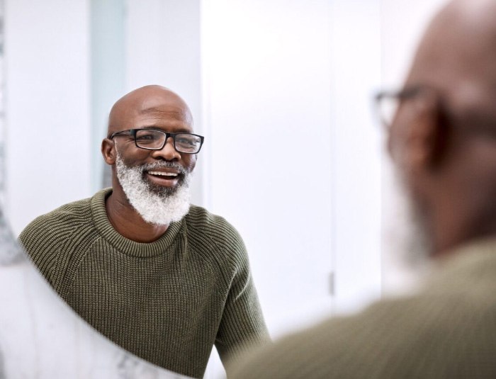 Senior man in dark green sweater smiling at his reflection