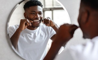 Man smiling in mirror while flossing his teeth
